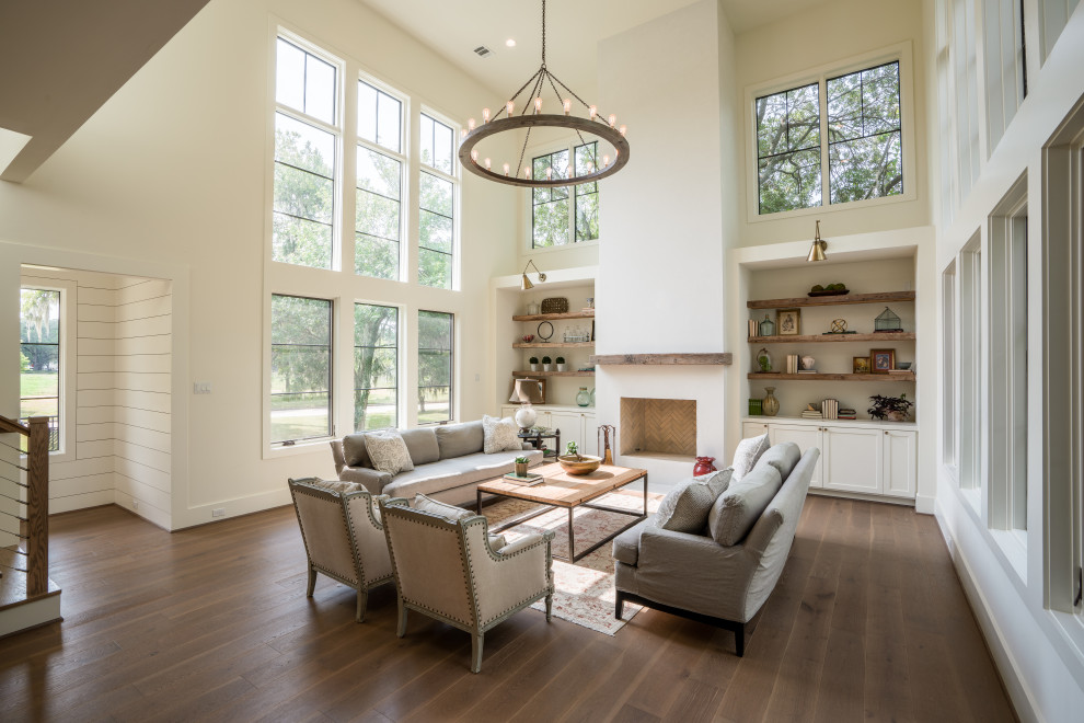 Large country open plan games room in Houston with a reading nook, white walls, medium hardwood flooring, a standard fireplace, a plastered fireplace surround, a concealed tv, brown floors and exposed beams.