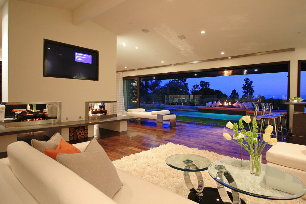 Diseño de sala de estar abierta minimalista con paredes beige, suelo de madera oscura, chimenea de doble cara, marco de chimenea de metal, televisor colgado en la pared y alfombra