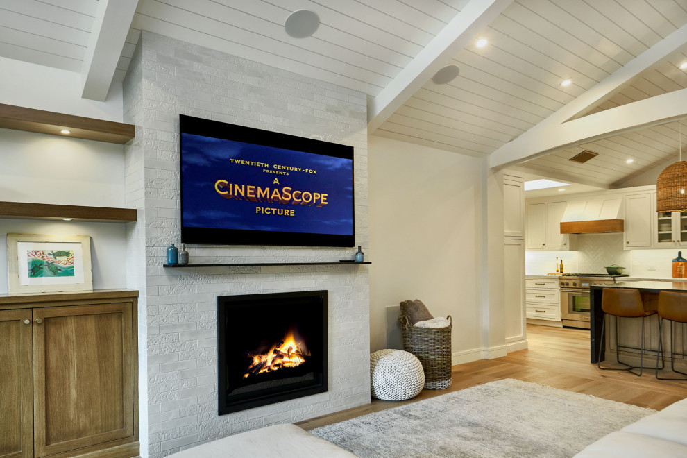 Example of a large transitional open concept light wood floor, gray floor and vaulted ceiling family room design in San Francisco with white walls, a standard fireplace, a brick fireplace and a wall-mounted tv