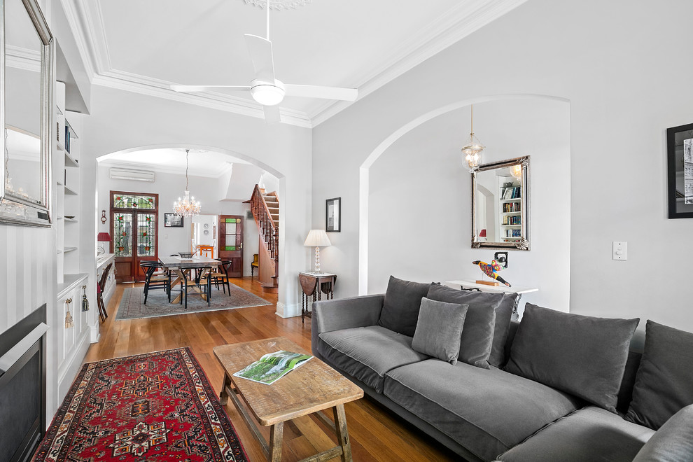 Cette photo montre une salle de séjour victorienne ouverte avec un mur blanc, un sol en bois brun, une cheminée standard et aucun téléviseur.