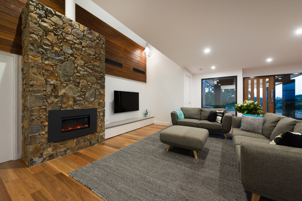 Réalisation d'une grande salle de séjour design ouverte avec un mur blanc, un sol en bois brun, une cheminée standard, un manteau de cheminée en pierre et un téléviseur encastré.