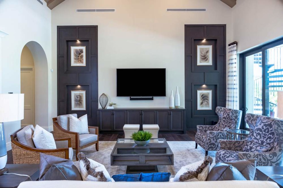 Imagen de sala de estar con biblioteca abierta mediterránea grande con paredes beige, suelo de madera oscura, televisor colgado en la pared y suelo marrón