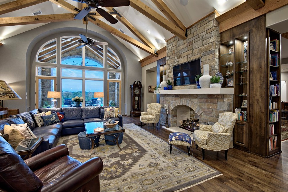This is an example of a large classic open plan games room in Austin with beige walls, dark hardwood flooring, a two-sided fireplace, a stone fireplace surround and a wall mounted tv.