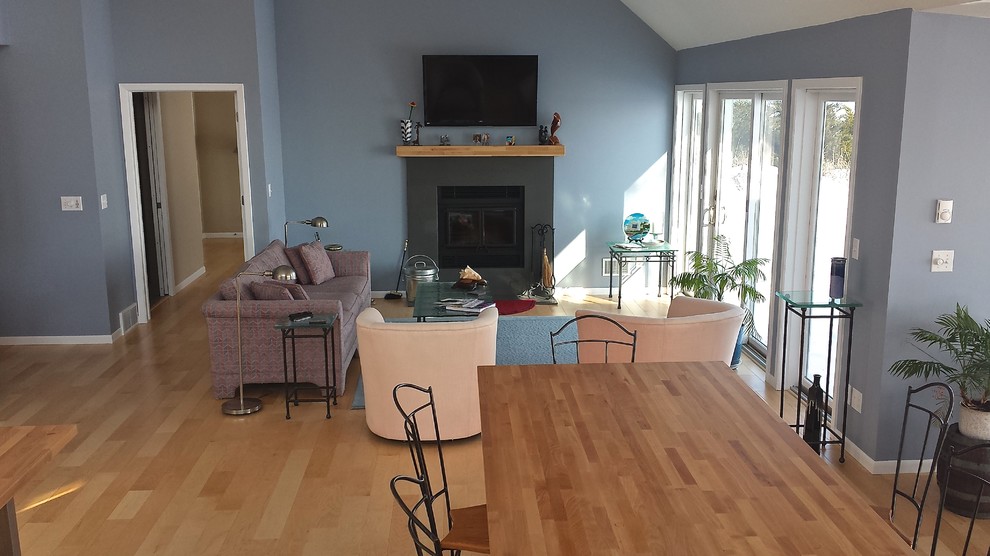 Ejemplo de sala de estar abierta costera de tamaño medio con paredes azules, suelo de madera clara, todas las chimeneas, marco de chimenea de piedra y televisor colgado en la pared