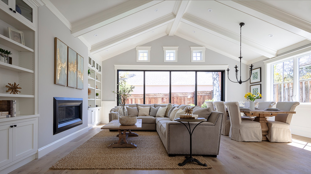 Diseño de sala de estar abierta campestre pequeña con paredes grises, suelo de madera clara, chimenea de doble cara, marco de chimenea de yeso, televisor colgado en la pared, suelo gris y alfombra