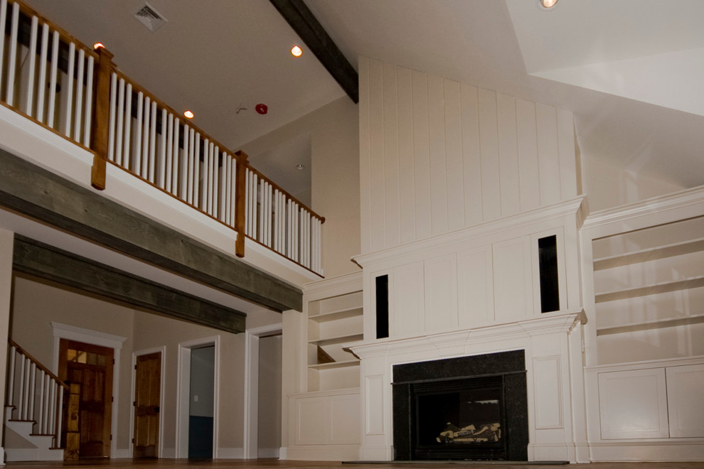 Foto de sala de estar tipo loft de estilo de casa de campo con chimeneas suspendidas, suelo de madera en tonos medios, marco de chimenea de piedra, televisor retractable y paredes beige