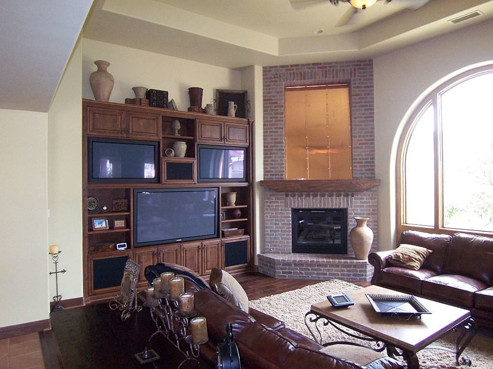 Design ideas for a large mediterranean open plan games room in Other with beige walls, a corner fireplace, a brick fireplace surround, a built-in media unit and medium hardwood flooring.