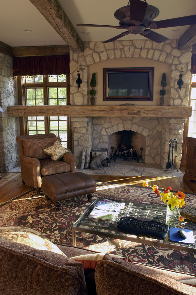 Imagen de sala de estar cerrada rural extra grande con paredes beige, suelo de madera en tonos medios, todas las chimeneas, marco de chimenea de piedra y televisor colgado en la pared