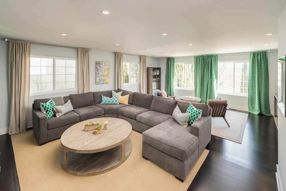 Diseño de sala de estar abierta contemporánea grande sin chimenea con paredes grises, suelo de madera oscura y televisor colgado en la pared