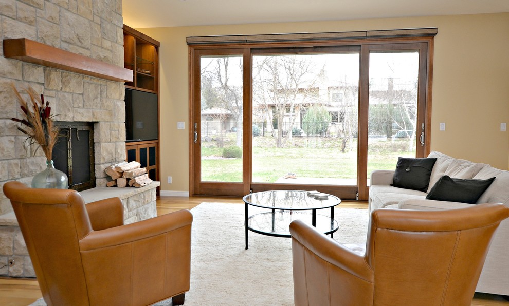 Mittelgroßes, Offenes Rustikales Wohnzimmer mit gelber Wandfarbe, hellem Holzboden, Kamin, Kaminumrandung aus Stein und freistehendem TV in Boise