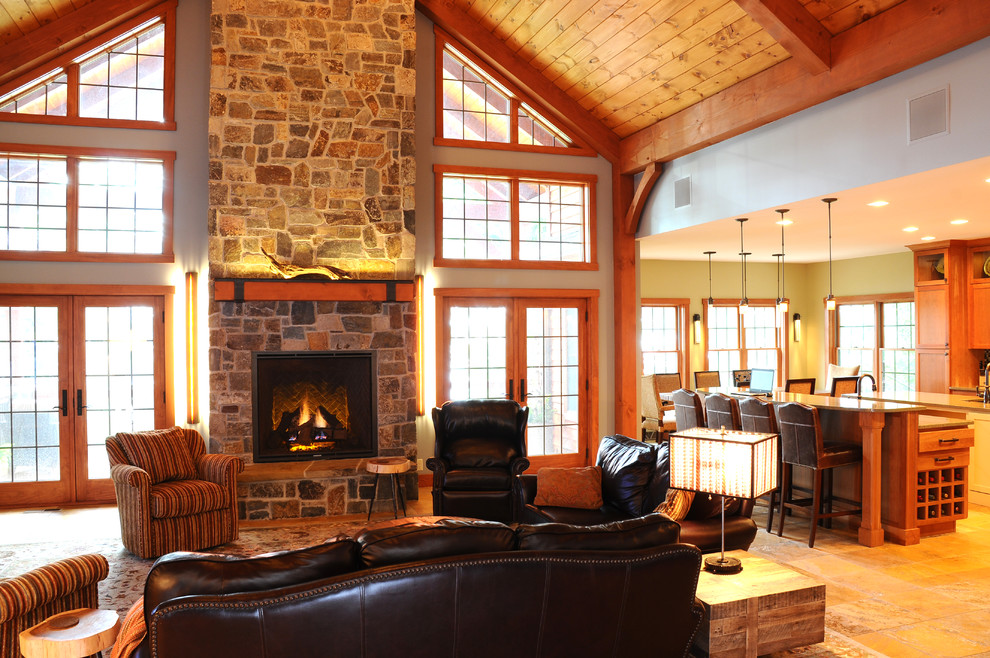 Cette photo montre une grande salle de séjour montagne ouverte avec un bar de salon, un mur bleu, un sol en travertin, une cheminée standard, un manteau de cheminée en pierre et aucun téléviseur.