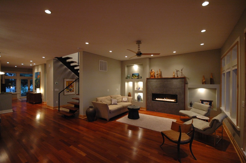 Ejemplo de sala de estar abierta actual con suelo de madera en tonos medios, chimenea lineal y marco de chimenea de baldosas y/o azulejos
