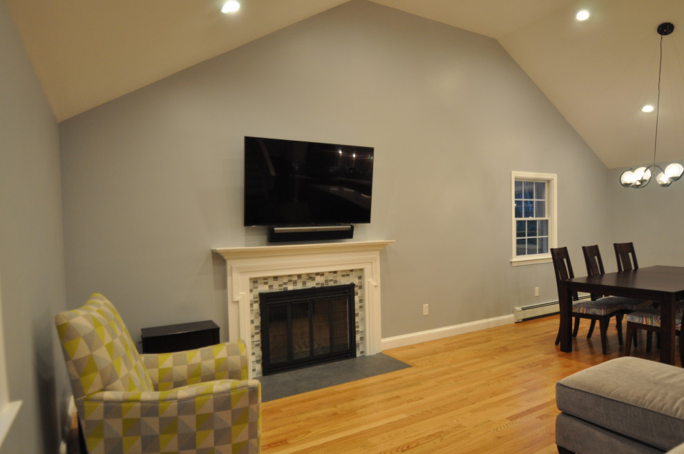 Ejemplo de sala de estar abierta y abovedada ecléctica de tamaño medio con paredes grises, suelo de madera clara, todas las chimeneas, marco de chimenea de baldosas y/o azulejos y suelo marrón