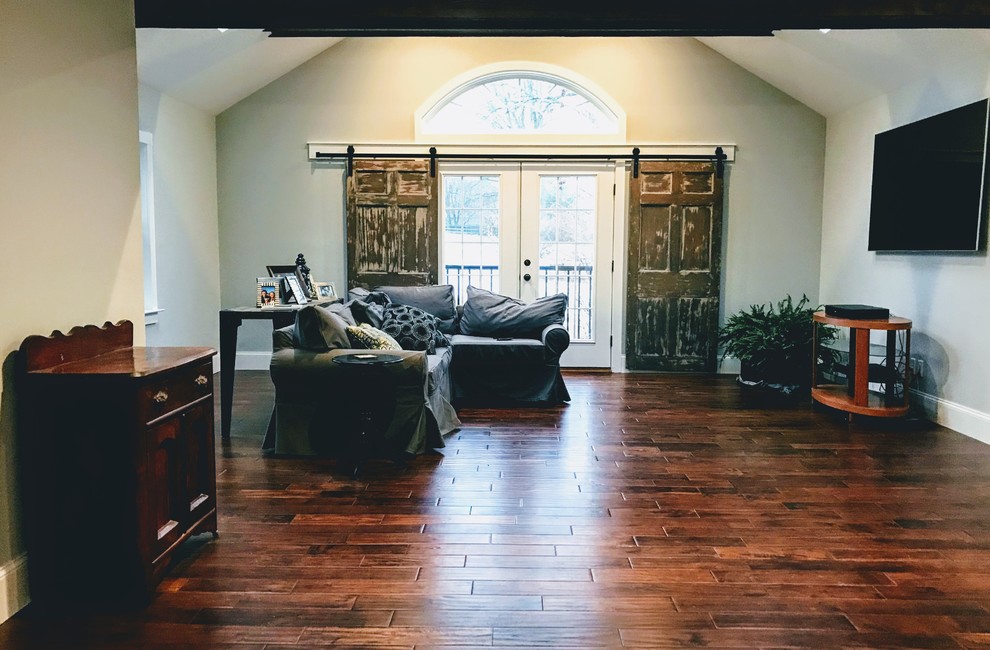 Пример оригинального дизайна: открытая гостиная комната среднего размера в стиле кантри с с книжными шкафами и полками, серыми стенами, паркетным полом среднего тона, телевизором на стене и коричневым полом без камина
