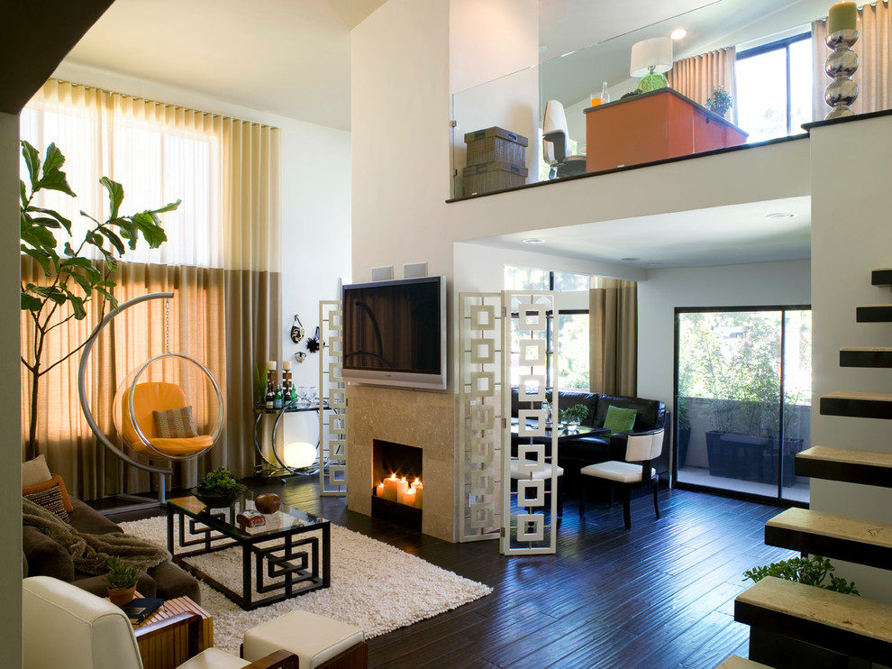 На фото: открытая гостиная комната в современном стиле с желтыми стенами, темным паркетным полом, стандартным камином, фасадом камина из камня и телевизором на стене