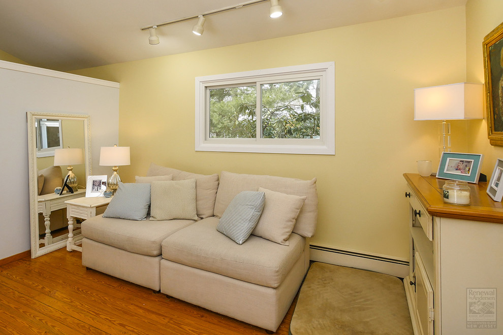 Imagen de sala de estar con biblioteca abierta costera de tamaño medio sin chimenea y televisor con paredes amarillas, suelo de madera en tonos medios y suelo marrón