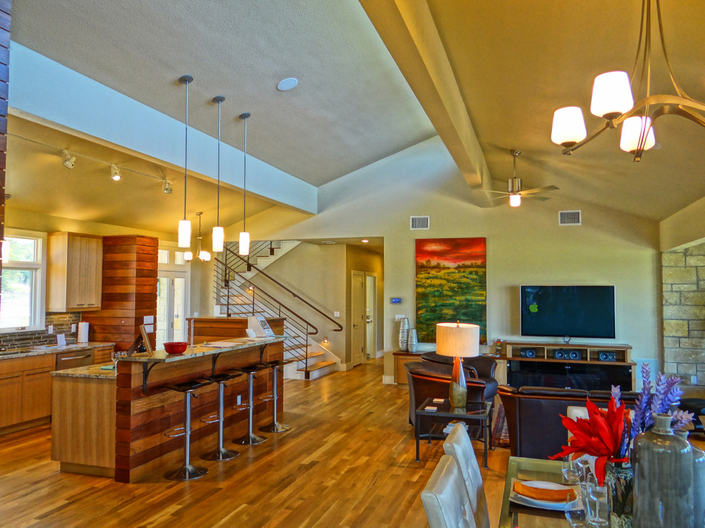 Großes, Offenes Modernes Wohnzimmer mit Hausbar, beiger Wandfarbe, hellem Holzboden, Eckkamin, Kaminumrandung aus Stein, freistehendem TV und braunem Boden in Austin