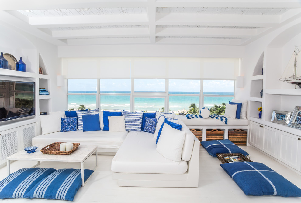 На фото: гостиная комната в морском стиле с белыми стенами, деревянным полом, мультимедийным центром и белым полом с