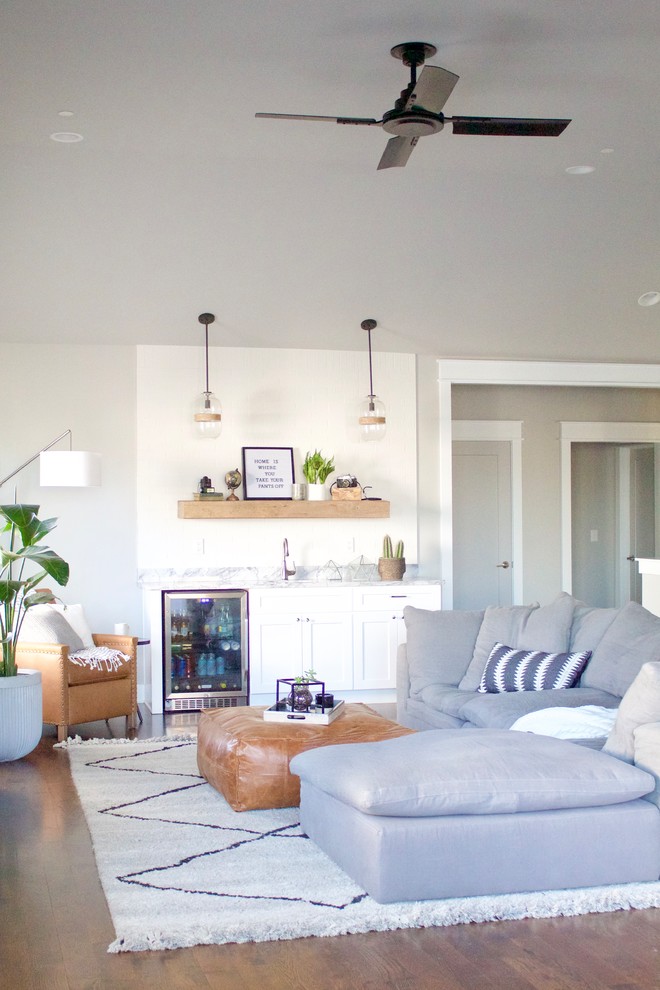 На фото: большая открытая гостиная комната в стиле модернизм с домашним баром, серыми стенами, темным паркетным полом, телевизором на стене и коричневым полом без камина