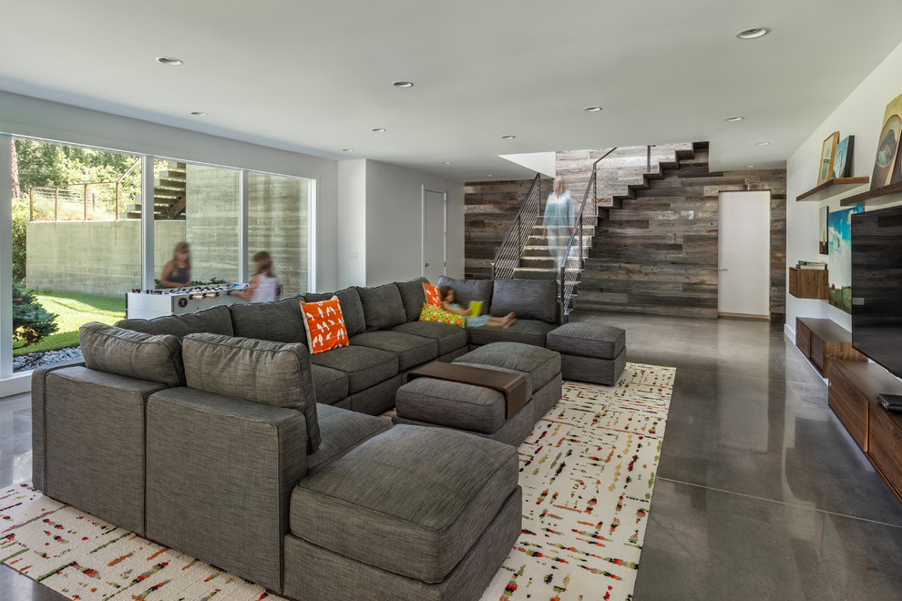 Esempio di un grande soggiorno design aperto con pareti bianche, pavimento in cemento, TV a parete, sala giochi e tappeto