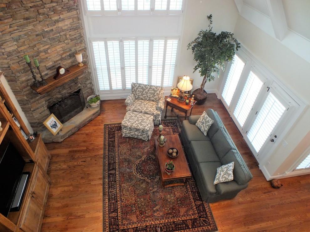 Foto de sala de estar tipo loft tradicional grande con paredes beige, suelo de madera oscura, chimenea de esquina, marco de chimenea de piedra, televisor independiente y suelo marrón