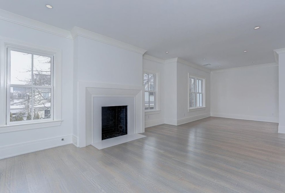 Photo of an expansive classic open plan games room in New York with white walls, light hardwood flooring, a standard fireplace and a plastered fireplace surround.