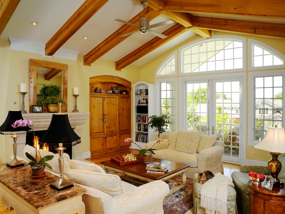 Diseño de sala de estar tradicional con paredes amarillas, suelo de madera en tonos medios, todas las chimeneas y marco de chimenea de piedra