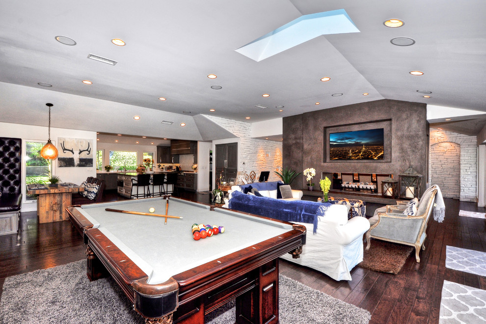Inspiration for an expansive classic open plan games room in Orange County with a game room, a two-sided fireplace, white walls, dark hardwood flooring, a concrete fireplace surround, a wall mounted tv and brown floors.