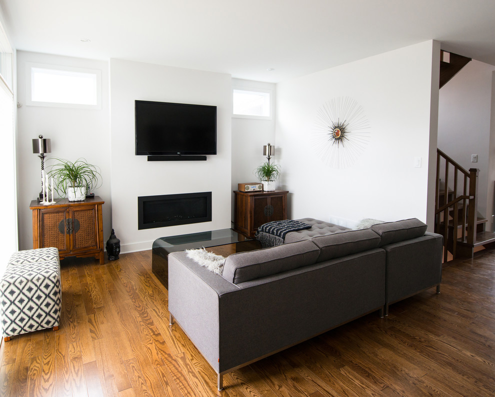Foto på ett funkis allrum, med vita väggar, mellanmörkt trägolv, en bred öppen spis och en väggmonterad TV
