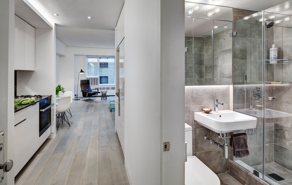 Cette photo montre une petite salle de séjour moderne ouverte avec un bar de salon, un mur blanc, parquet clair et un sol gris.