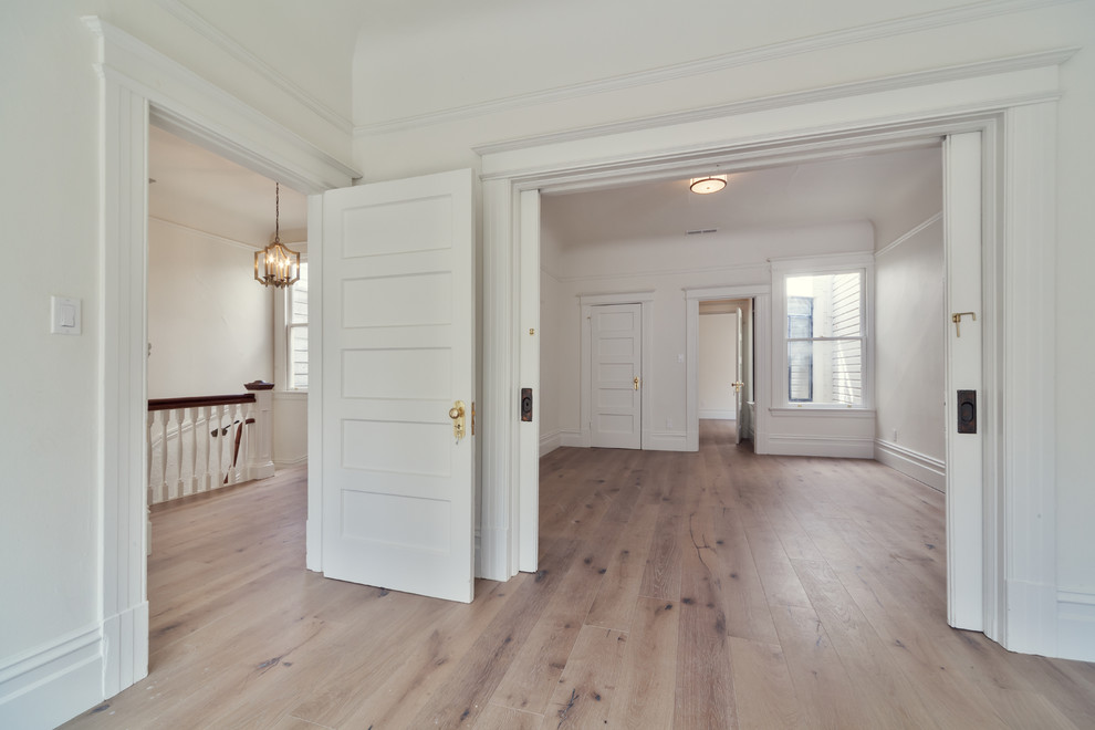 Idée de décoration pour une grande salle de séjour victorienne avec un mur blanc, parquet clair et un manteau de cheminée en bois.