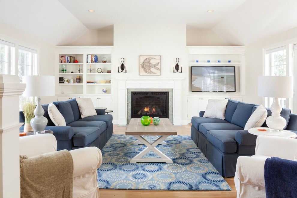 Свежая идея для дизайна: гостиная комната в морском стиле с с книжными шкафами и полками, белыми стенами, светлым паркетным полом, стандартным камином, фасадом камина из дерева и синим диваном - отличное фото интерьера