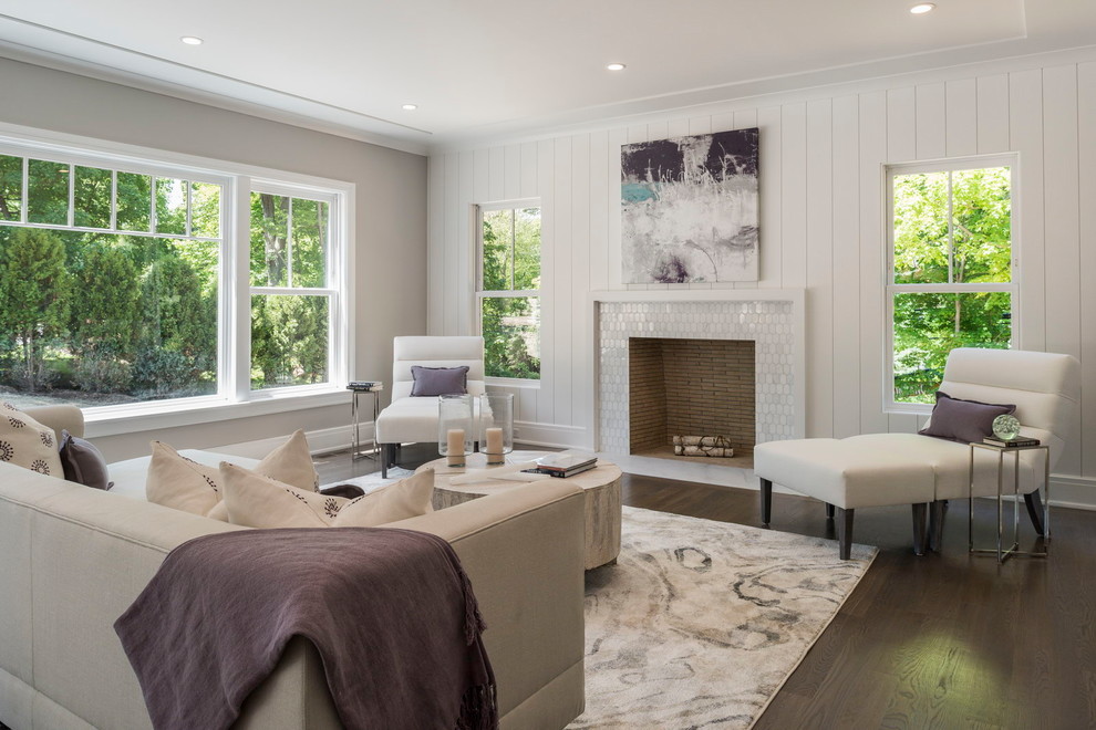 На фото: гостиная комната в стиле неоклассика (современная классика) с белыми стенами, темным паркетным полом, стандартным камином, фасадом камина из плитки и коричневым полом с