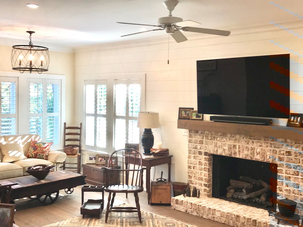 Design ideas for a country games room in Charleston with white walls, dark hardwood flooring, a standard fireplace, a brick fireplace surround, a wall mounted tv and brown floors.