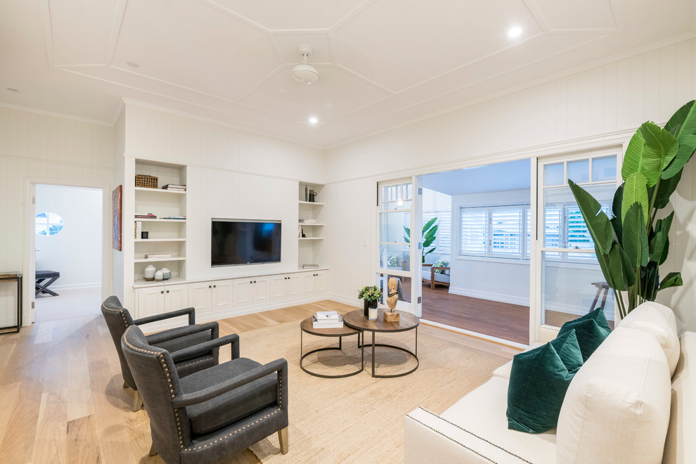 Diseño de sala de estar clásica grande con paredes blancas, suelo de madera clara, televisor colgado en la pared y suelo beige