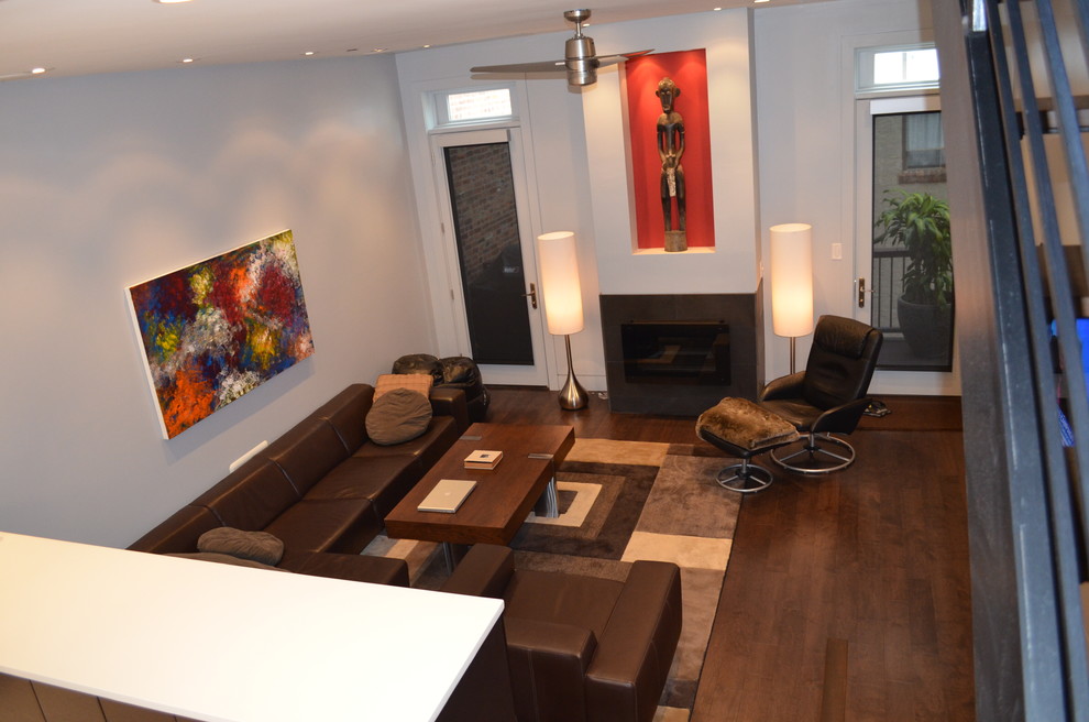 На фото: большая открытая гостиная комната в современном стиле с серыми стенами, темным паркетным полом, стандартным камином, фасадом камина из плитки и телевизором на стене