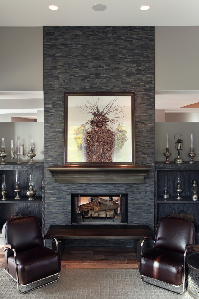 グランドラピッズにある広いコンテンポラリースタイルのおしゃれなファミリールーム (グレーの壁、無垢フローリング、標準型暖炉、石材の暖炉まわり) の写真
