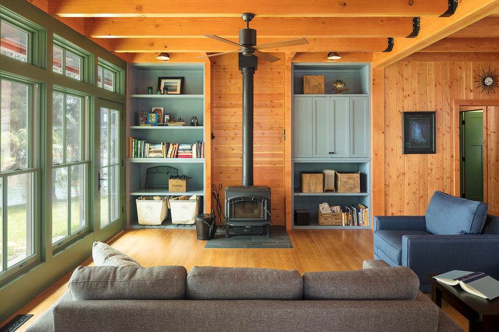 Modelo de sala de estar abierta rural con suelo de madera en tonos medios, estufa de leña y televisor retractable