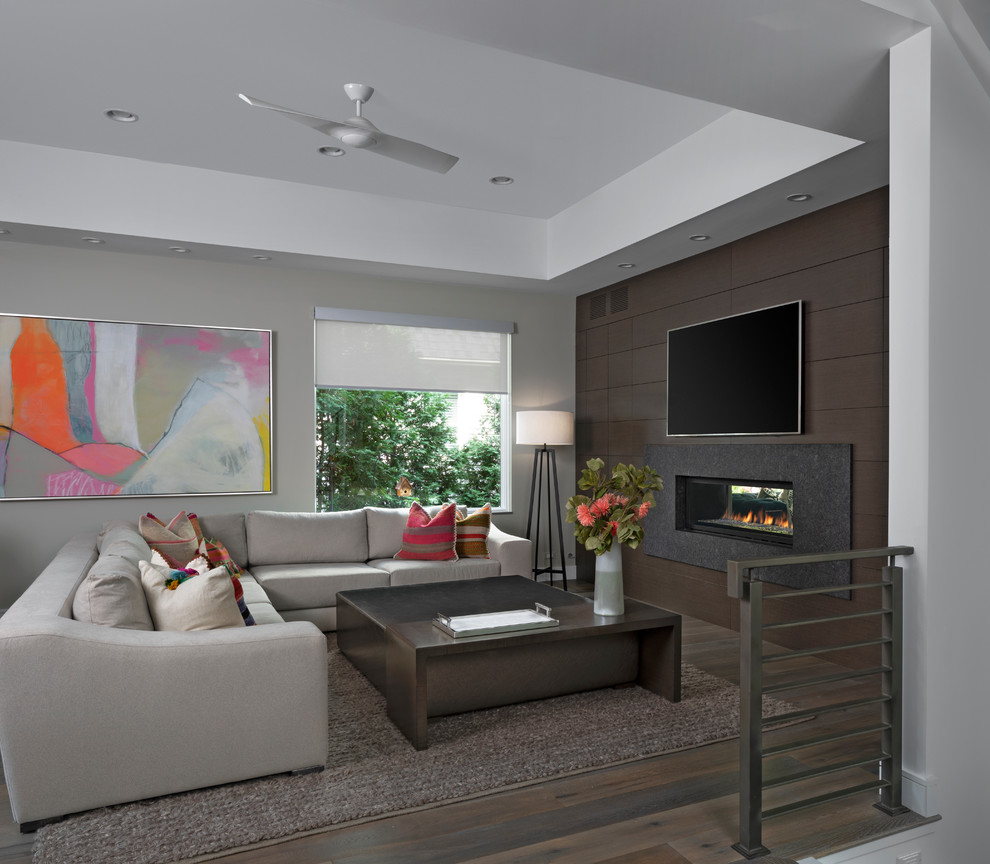 Cette image montre une grande salle de séjour design ouverte avec un mur gris, parquet foncé, un manteau de cheminée en pierre, une cheminée ribbon, un téléviseur fixé au mur et un sol marron.