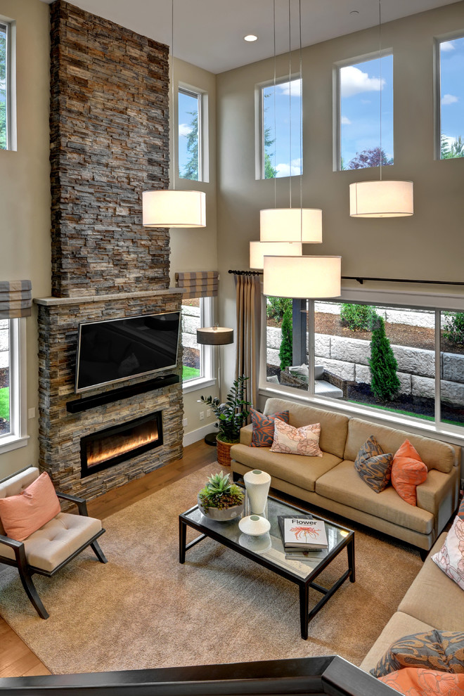 Modelo de sala de estar abierta clásica renovada con paredes grises, suelo de madera en tonos medios, todas las chimeneas, marco de chimenea de piedra, televisor colgado en la pared y alfombra