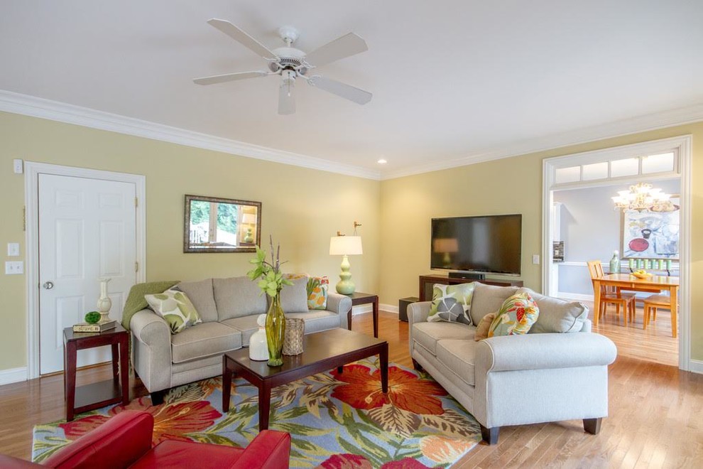 Foto de sala de estar cerrada tropical de tamaño medio sin chimenea con paredes beige, suelo de madera clara, televisor colgado en la pared y suelo marrón