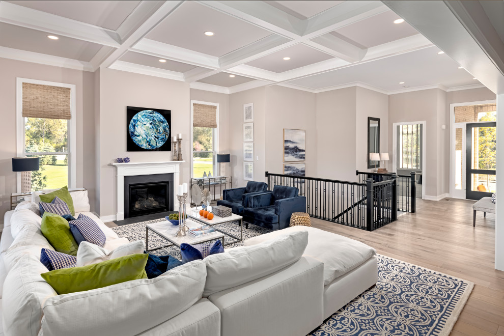 Пример оригинального дизайна: открытая гостиная комната в стиле неоклассика (современная классика) с серыми стенами, паркетным полом среднего тона, стандартным камином, коричневым полом и кессонным потолком
