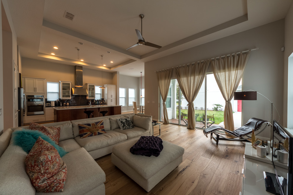 Großes, Offenes Modernes Wohnzimmer ohne Kamin mit hellem Holzboden, weißer Wandfarbe, freistehendem TV und beigem Boden in Orlando