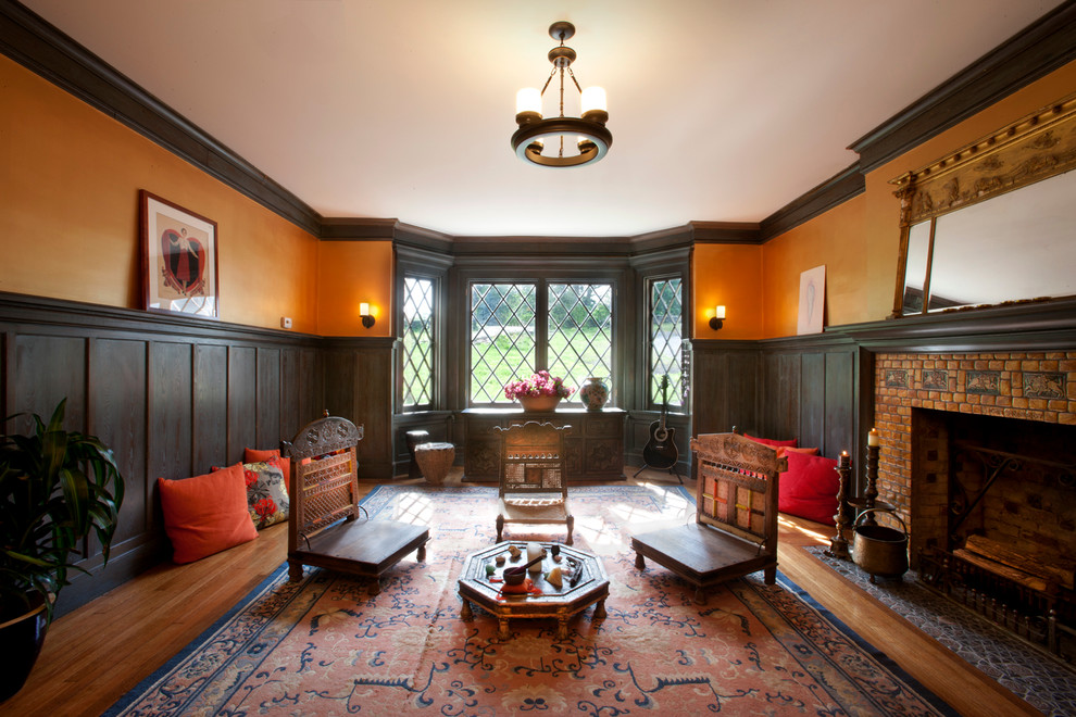 Стильный дизайн: гостиная комната в классическом стиле с оранжевыми стенами, паркетным полом среднего тона и стандартным камином - последний тренд