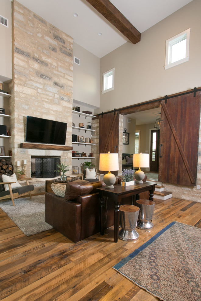 Example of a large cottage open concept medium tone wood floor and brown floor game room design in Austin with beige walls, a standard fireplace, a stone fireplace and a wall-mounted tv