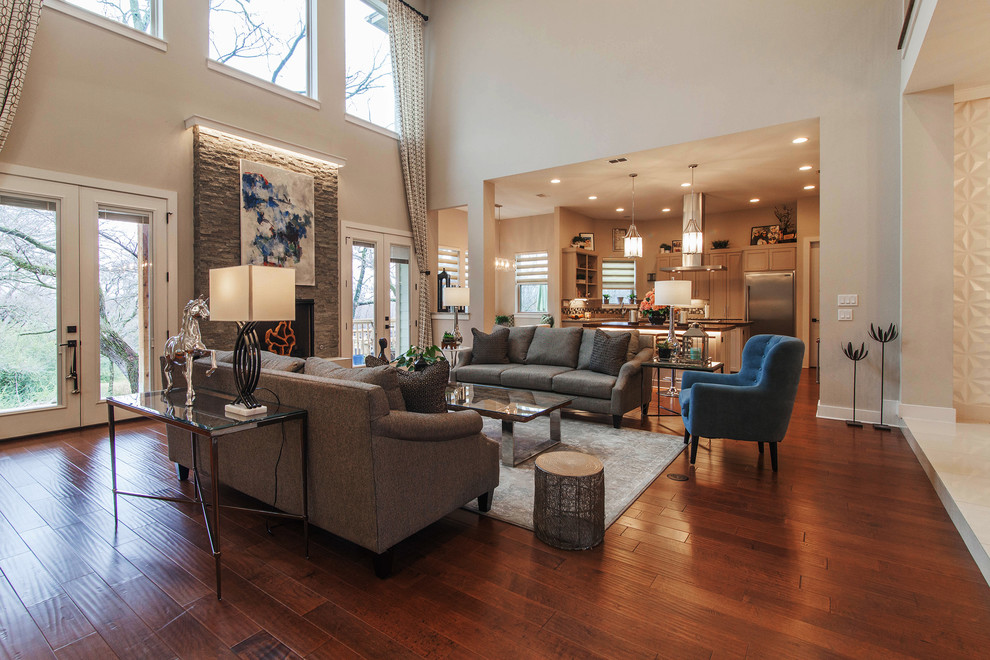 Imagen de sala de estar abierta contemporánea grande con paredes grises, suelo de madera en tonos medios, todas las chimeneas, marco de chimenea de piedra y suelo marrón
