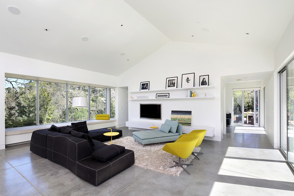 На фото: открытая гостиная комната среднего размера в современном стиле с белыми стенами, бетонным полом и телевизором на стене без камина