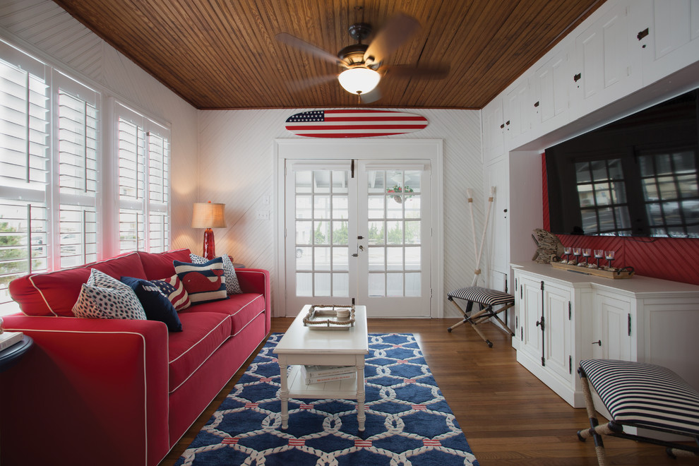 Imagen de sala de estar costera con paredes blancas, suelo de madera en tonos medios, televisor colgado en la pared y suelo marrón