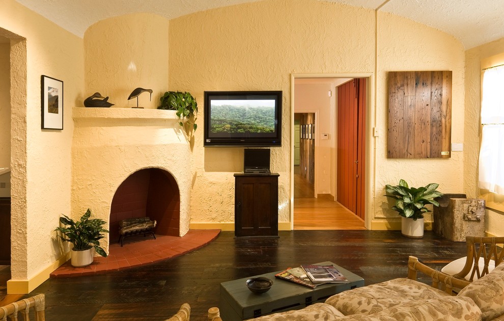 Imagen de sala de estar cerrada de estilo americano de tamaño medio con paredes amarillas, suelo de madera oscura, chimenea de esquina, marco de chimenea de yeso y televisor colgado en la pared