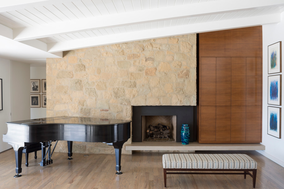 Cette image montre une salle de séjour design de taille moyenne et ouverte avec une salle de musique, un mur blanc, une cheminée standard, un sol en bois brun, un manteau de cheminée en pierre, un téléviseur dissimulé et un sol marron.